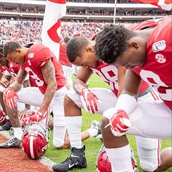 Football players kneel in prayer at the goal line at Bryant-Denny stadium